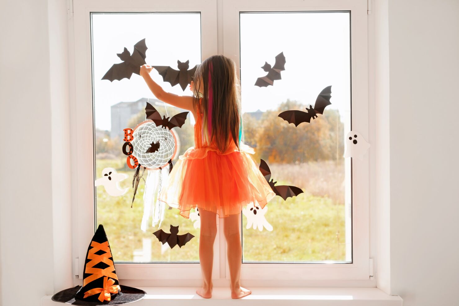 Ein Mädchen in einem orangen Kleid klebt Halloween Sticker an Fenster an