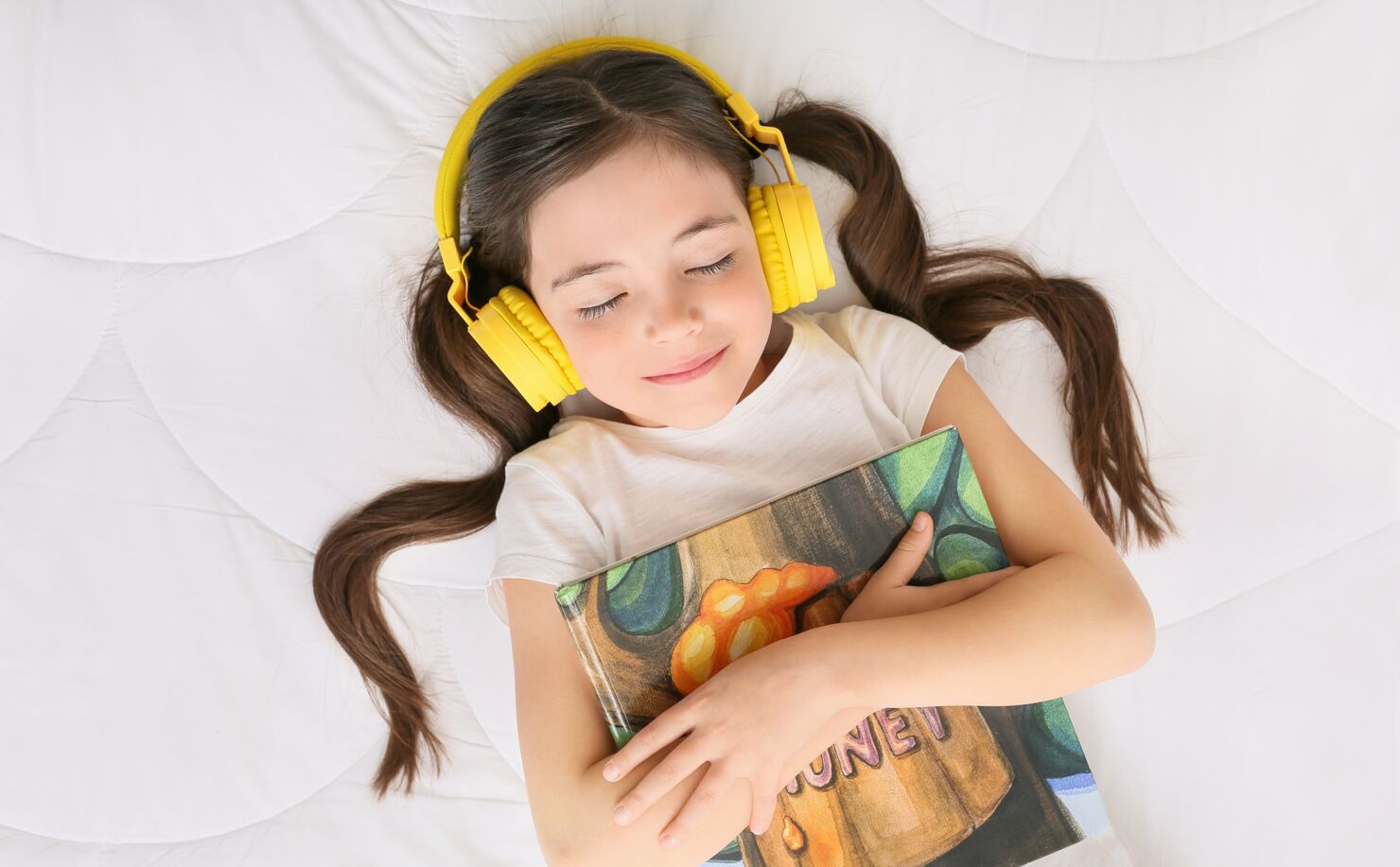 Ein Mädchen liegt auf einem Bett und hat Kopfhörer an, hört Musik und ihre Augen sind geschlossen